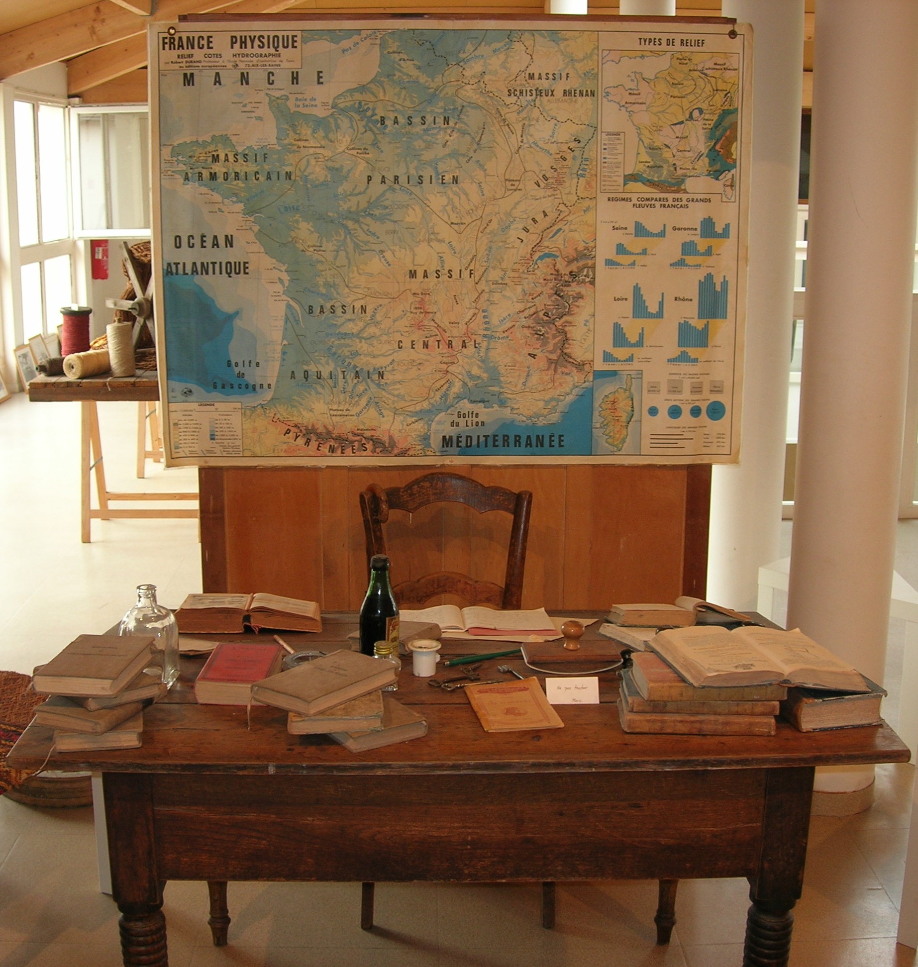 Salle d'exposition avec table d'écolier et carte de géographie ancienne